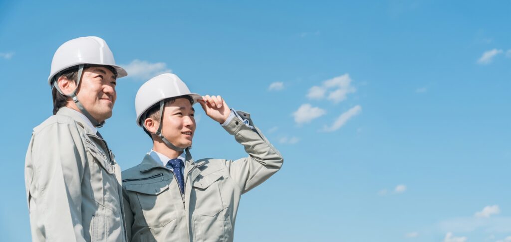 空を見上げる建設ヘルメットをかぶった2人の男性